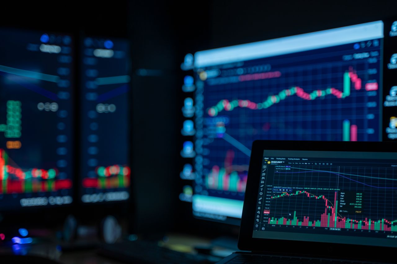Monitors showing charts and market data in a dimly lit room, the kind of dashboard where cold email reply rate metrics get read